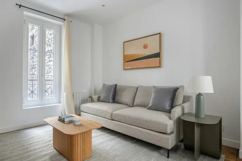 Salon clair d'un appartement rénové, canapé gris et parquet